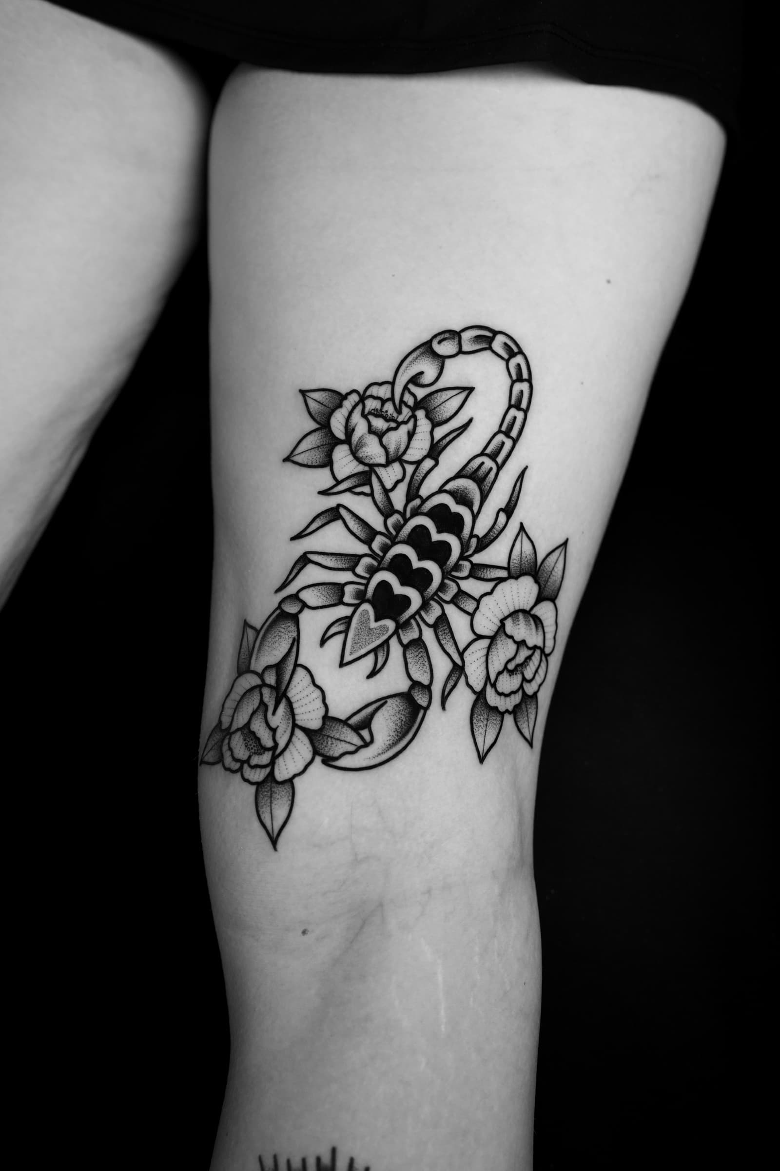 Tatouage traditionnel noir et gris d’un scorpion entouré de fleurs