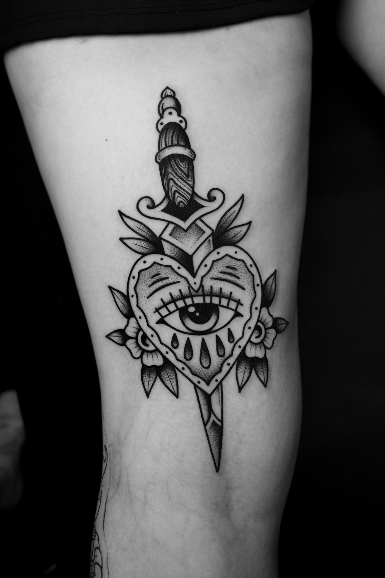 Tatouage noir et gris d’un cœur avec un œil traversé par une dague